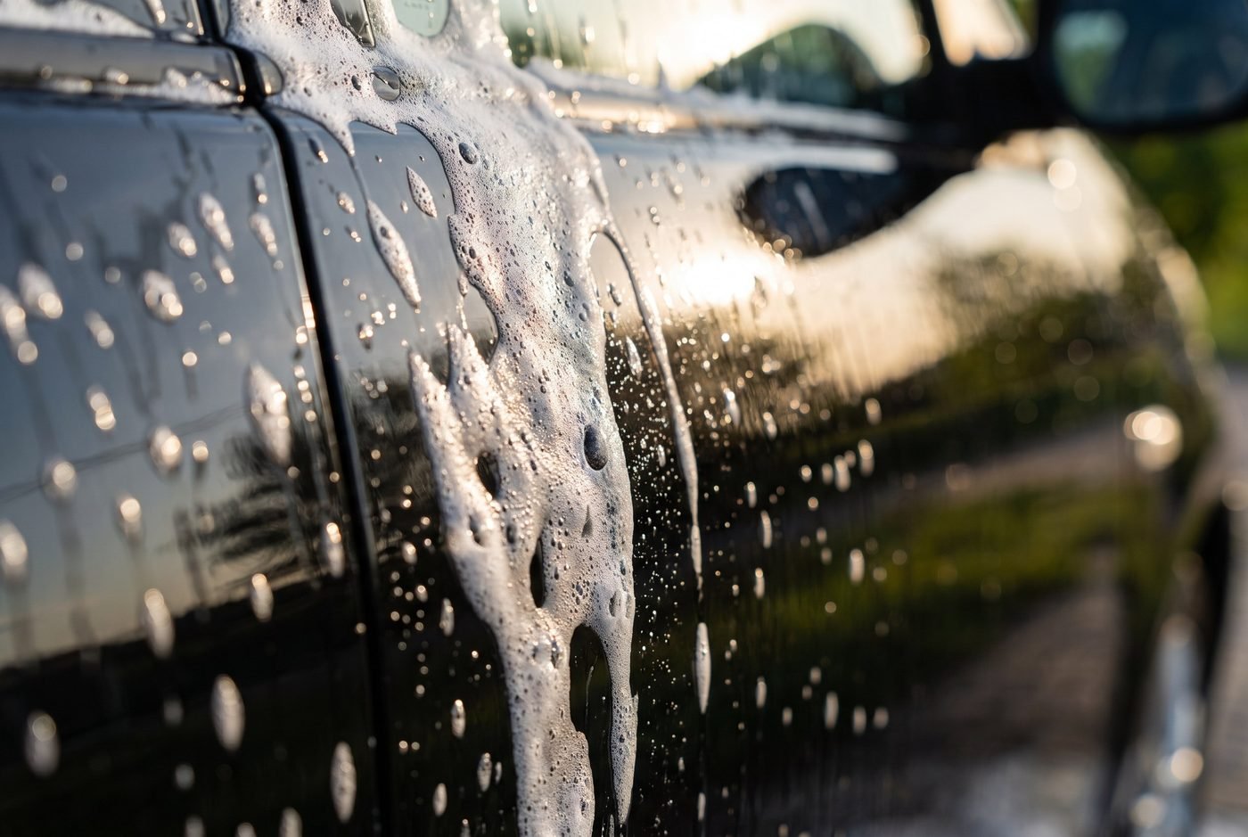 Thick white foam cascading down a glossy black car door panel during hand wash